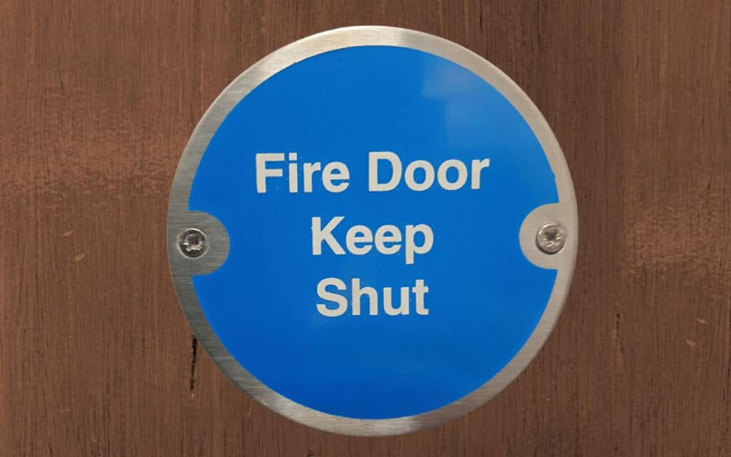 Round blue sign with the words Fire Door Keep Shut on wooden background